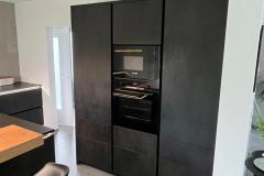 Hochschrank mit eingefrästen Griffen und schwarzen Elektro-Geräten